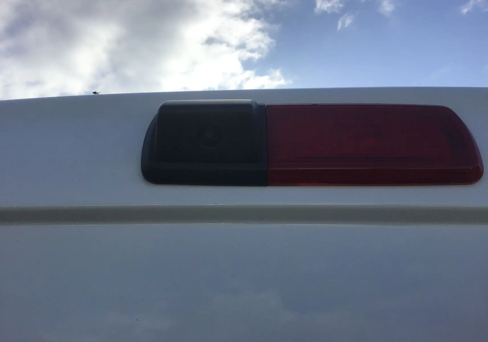 Gros plan sur la caméra de recul et le feu arrière rouge du Renault Trafic Fourgon blanc, vue arrière haute.