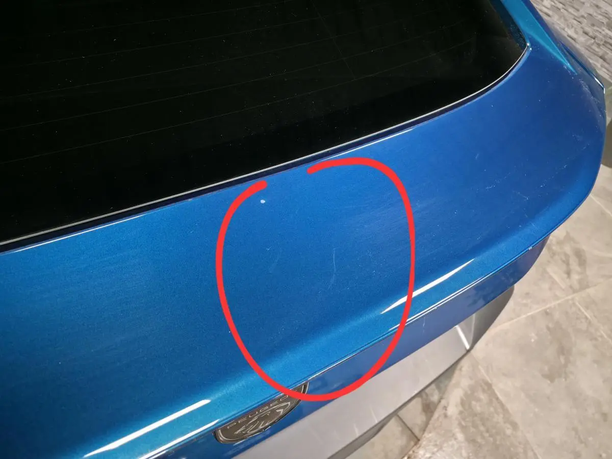 Détail du coffre arrière bleu métallisé d'une Peugeot 408 2024 avec rayures visibles au centre.