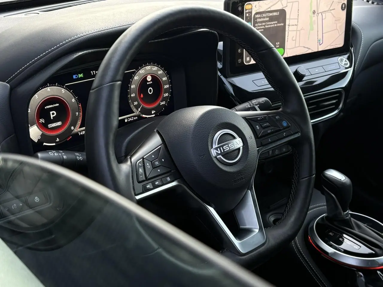 Vue intérieure centrée sur le volant Nissan et le combiné digital, avec écran tactile et levier de vitesse noir.