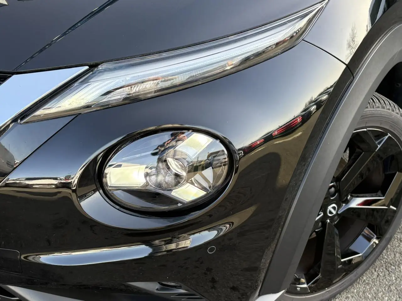 Gros plan sur le phare avant gauche et la jante noire du Nissan Juke 2024 Black Pearl, finition Tekna.