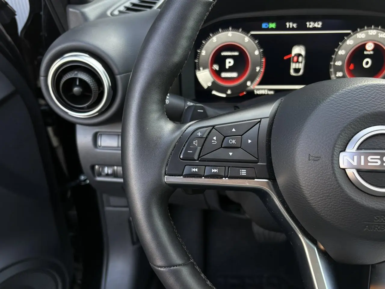Gros plan sur le volant noir du Nissan Juke 2024 avec commandes intégrées et tableau de bord digital lumineux.