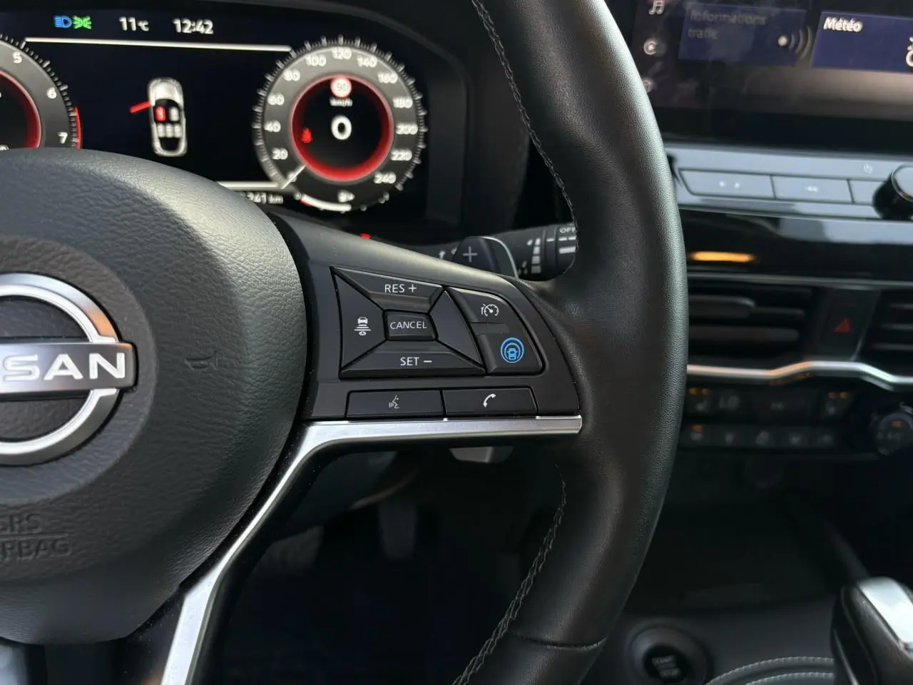 Gros plan sur le volant noir du Nissan Juke 2024 avec commandes de régulateur adaptatif et tableau de bord digital.