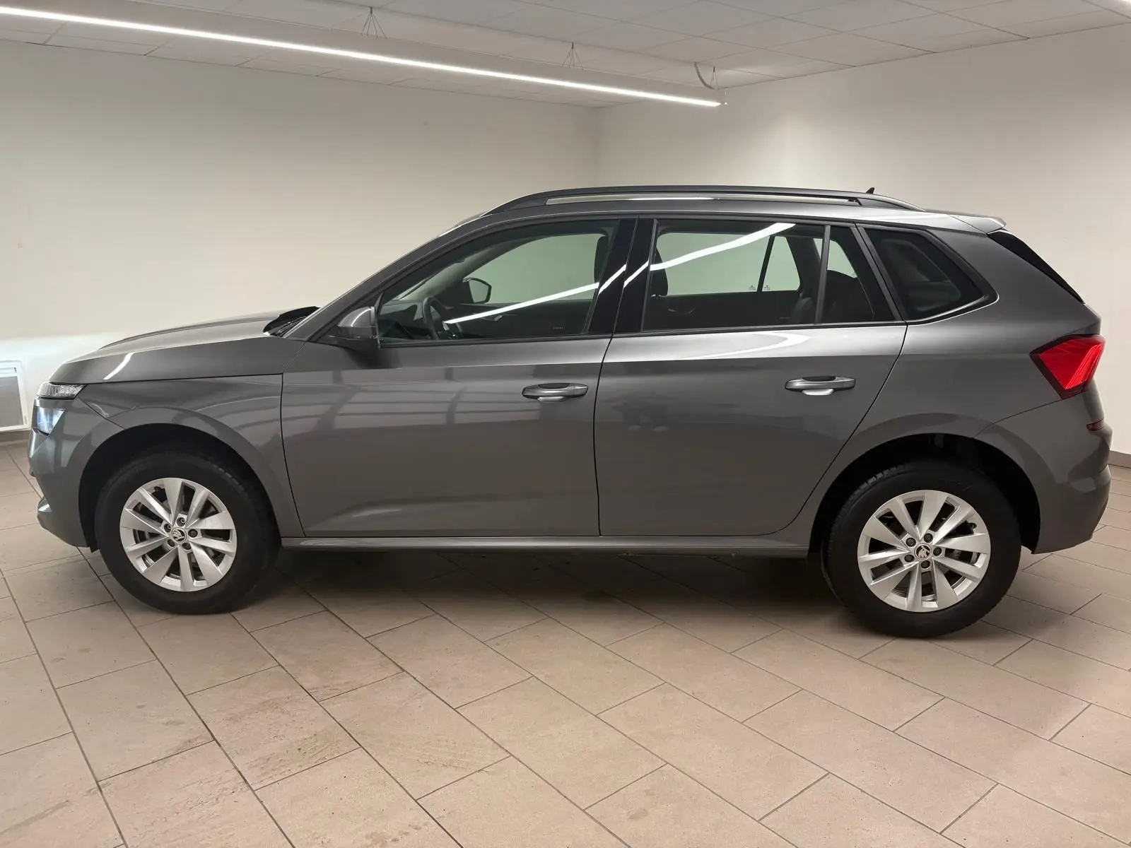 Vue de profil côté gauche d'un Skoda Kamiq 2023 gris graphite métallisé avec jantes alliage en intérieur neutre.