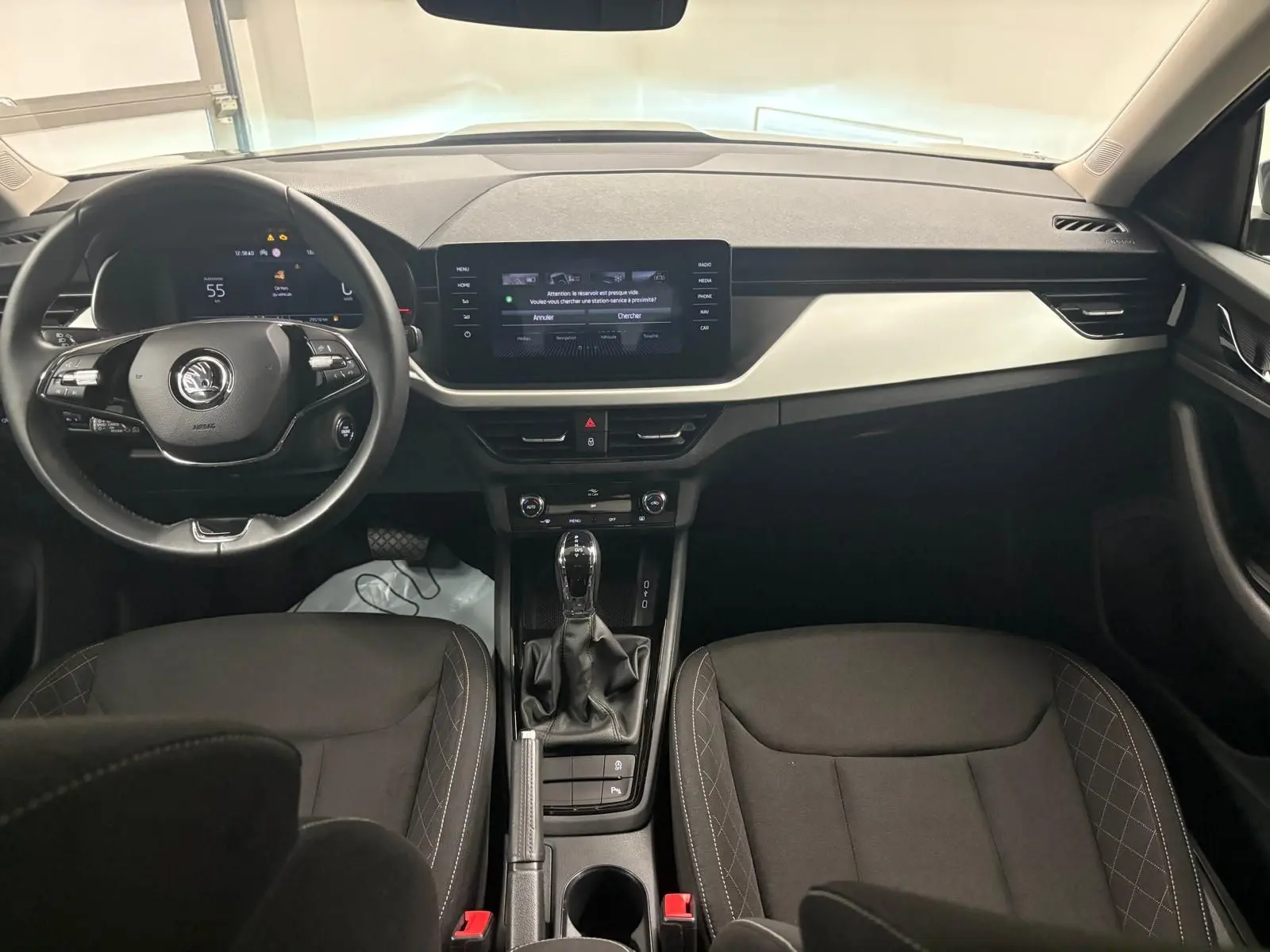 Intérieur du Skoda Kamiq 2023 vu de face, tableau de bord moderne avec écran tactile et sièges noirs à surpiqûres grises.