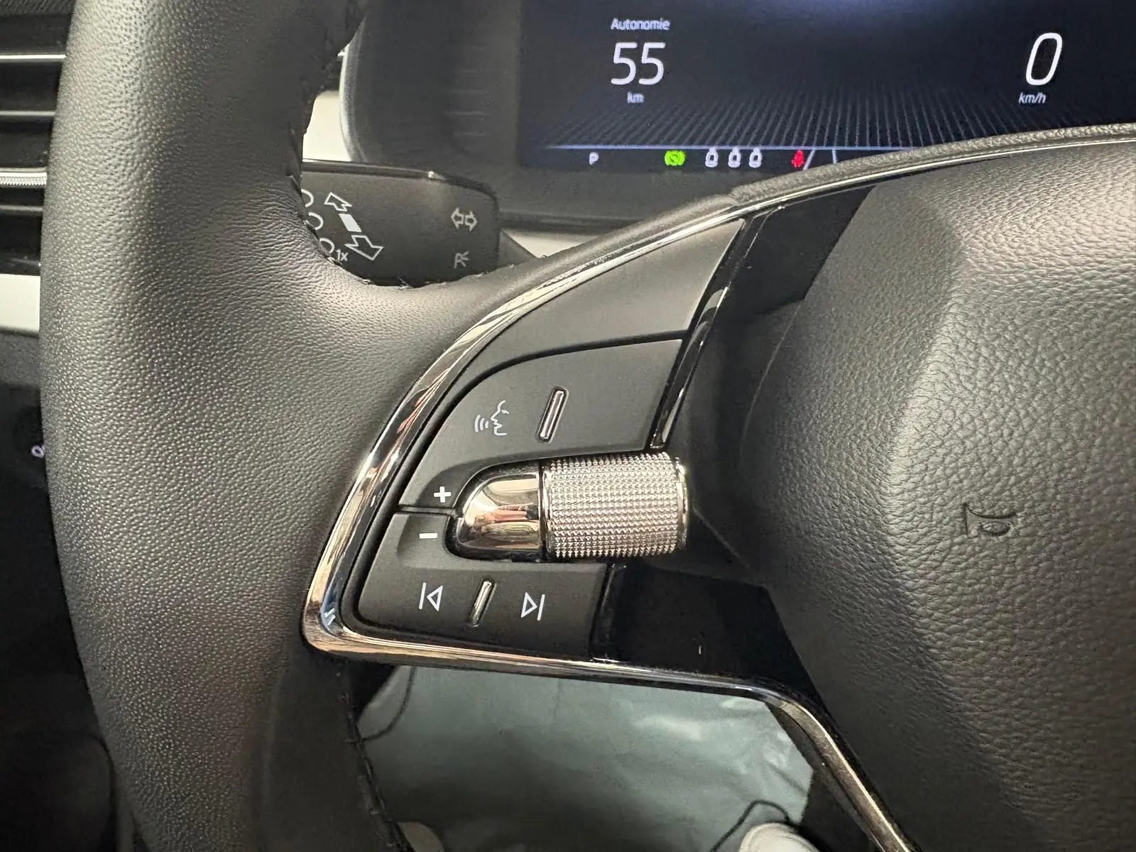 Gros plan sur les commandes gauche du volant du Skoda Kamiq 2023 gris graphite, avec affichage numérique en arrière-plan.