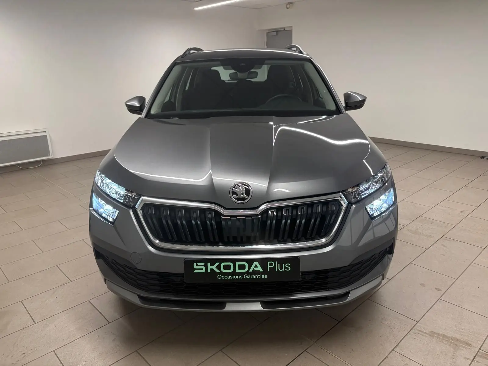 Vue avant d'un Skoda Kamiq 2023 gris graphite avec calandre noire et phares allumés en intérieur.