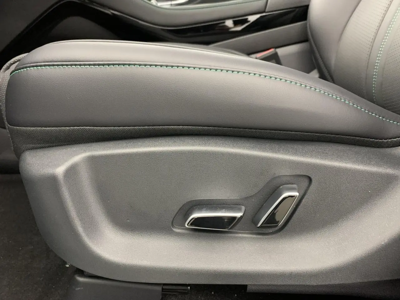 Détail des commandes électriques du siège avant côté gauche en cuir noir avec surpiqûres vertes du BYD SEAL U 2025.