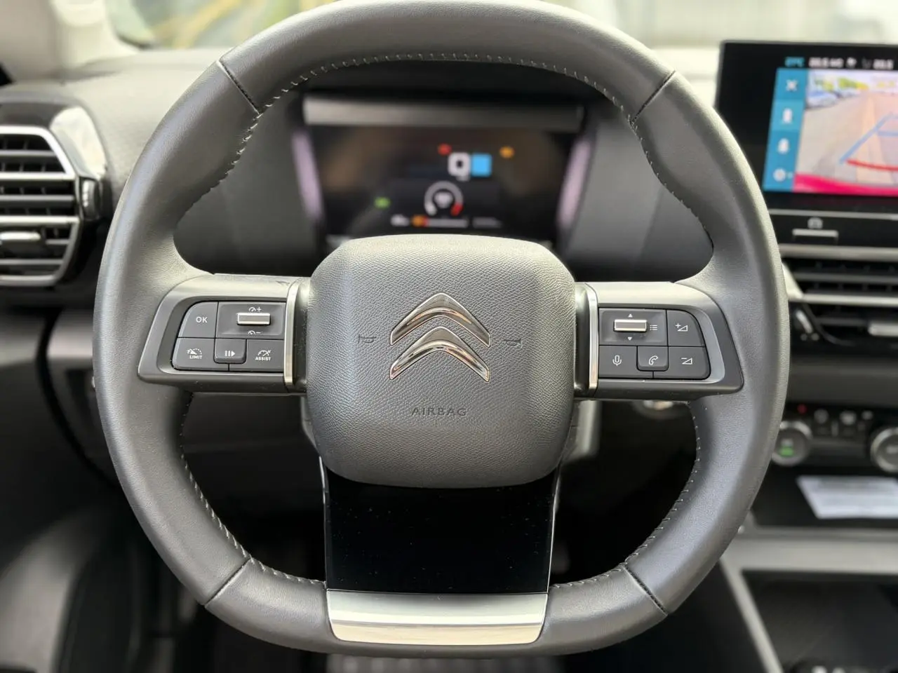 Vue rapprochée du volant en cuir noir avec commandes intégrées et tableau de bord numérique d'une Citroën C4 2024.