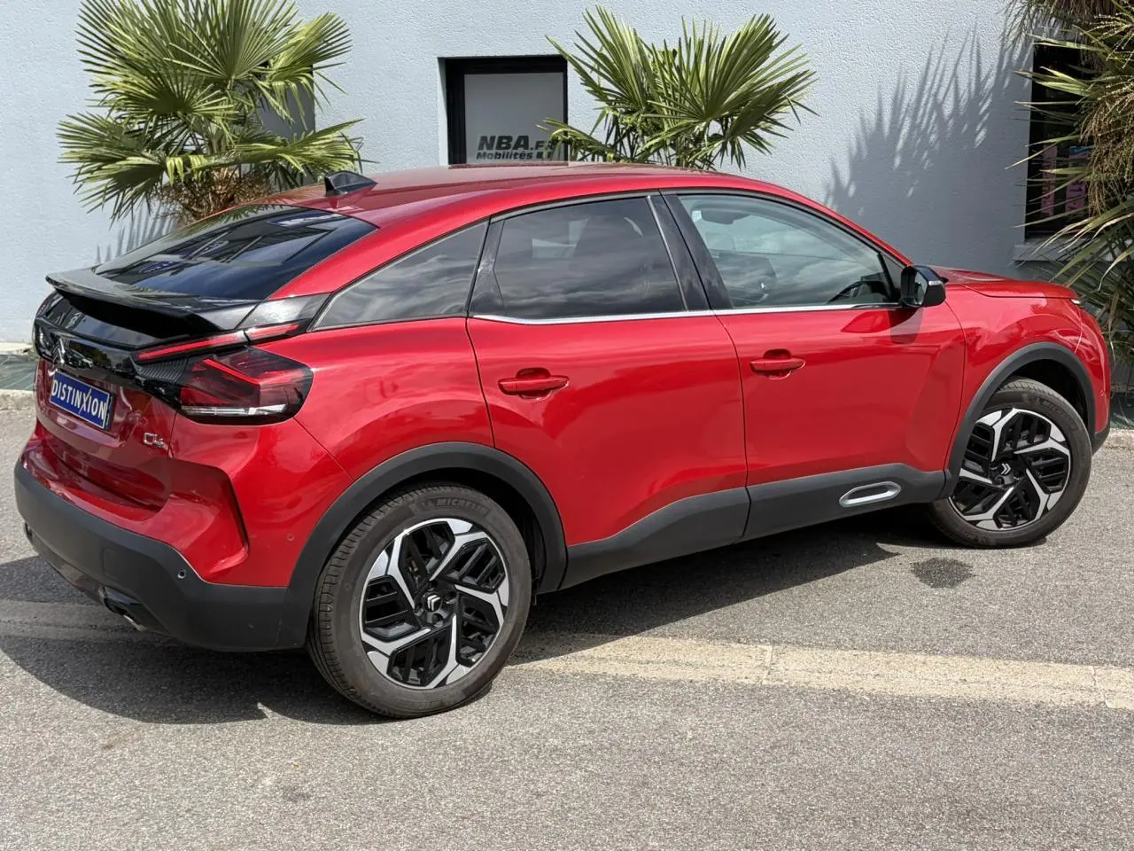 Vue 3/4 arrière droite d'une Citroën C4 2024 rouge Elixir avec jantes alliage noires et toit noir contrasté.