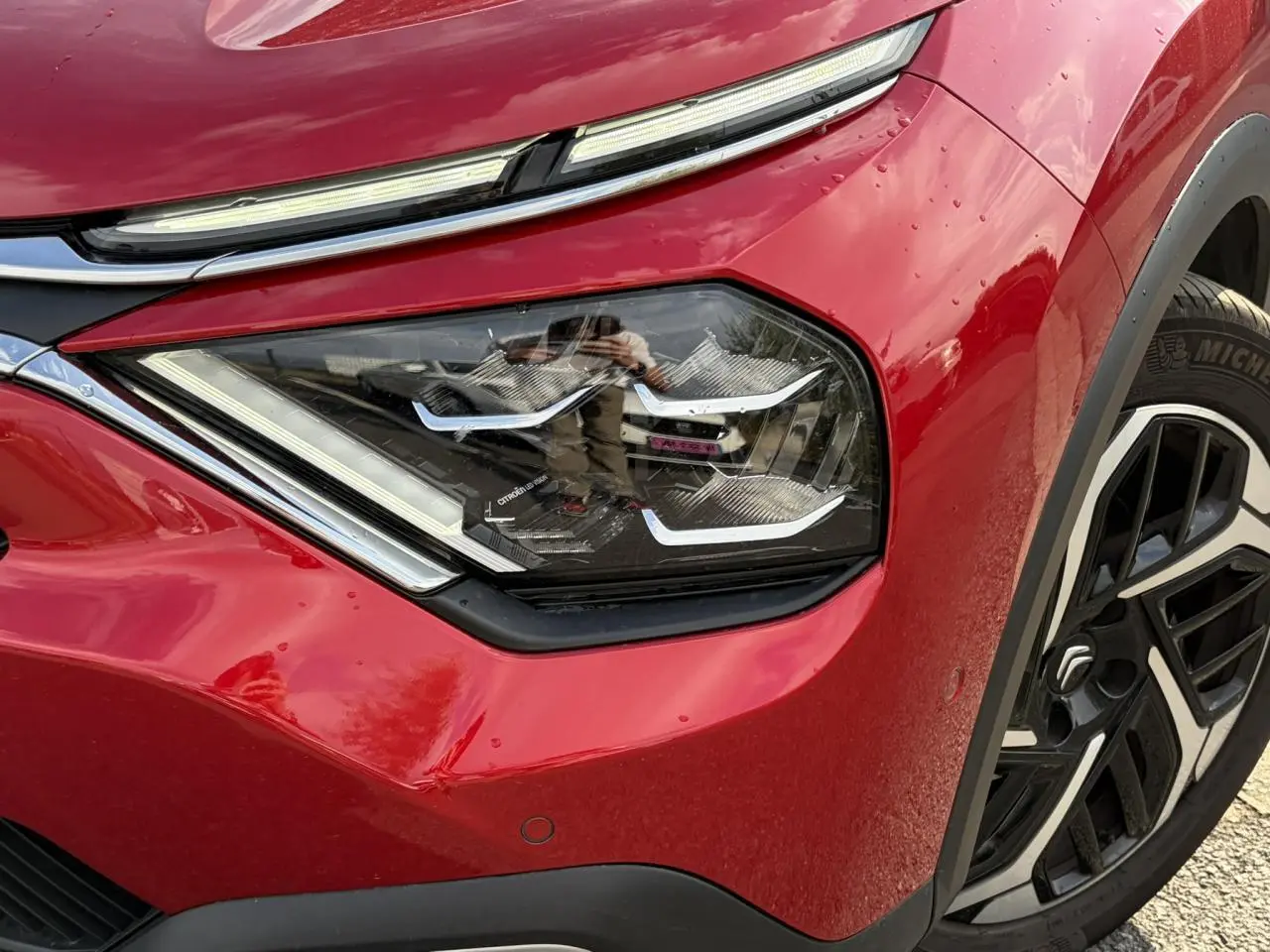 Gros plan sur le phare avant droit et la jante alliage noire et argent de la Citroën C4 Rouge Elixir 2024.