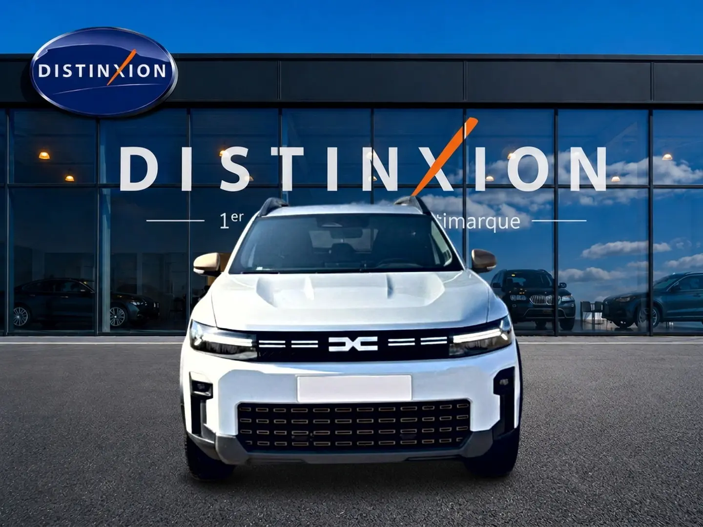 Vue avant d'un Dacia Bigster blanc avec calandre noire et logo DC, garé devant une vitrine Distinxion.