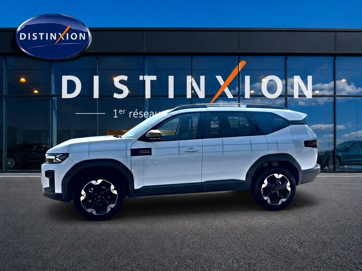 Profil droit du SUV blanc Dacia Bigster 2026 avec jantes noires et détails noirs contrastants, devant une vitrine Distinxion.