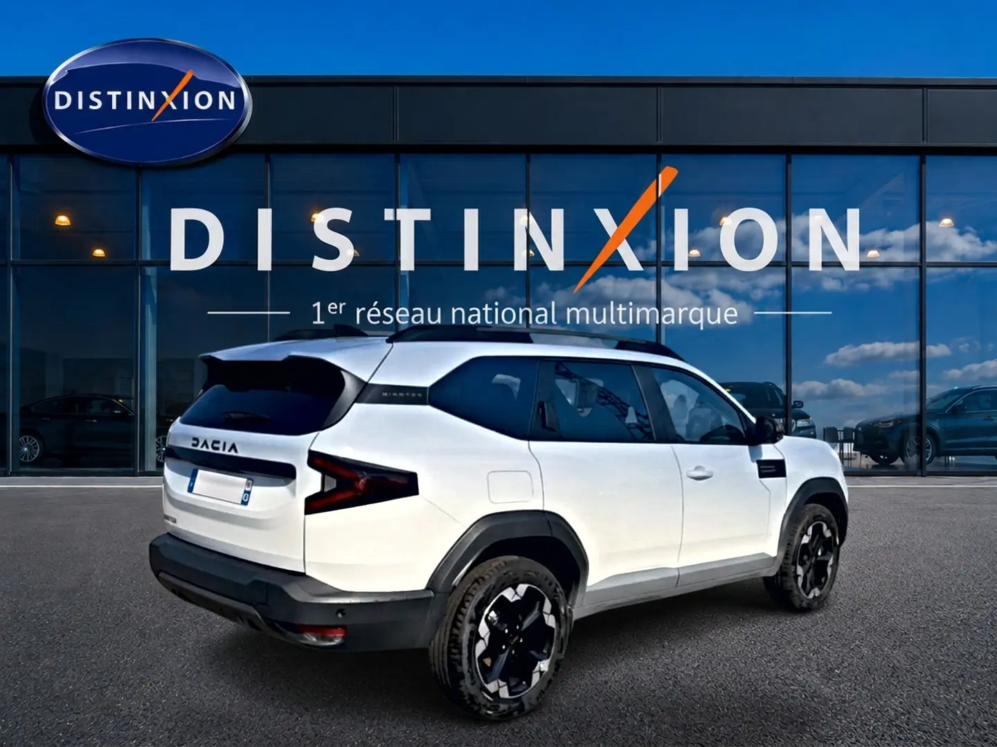 Vue 3/4 arrière droit du Dacia Bigster blanc avec jantes noires et toit noir devant une vitrine Distinxion.