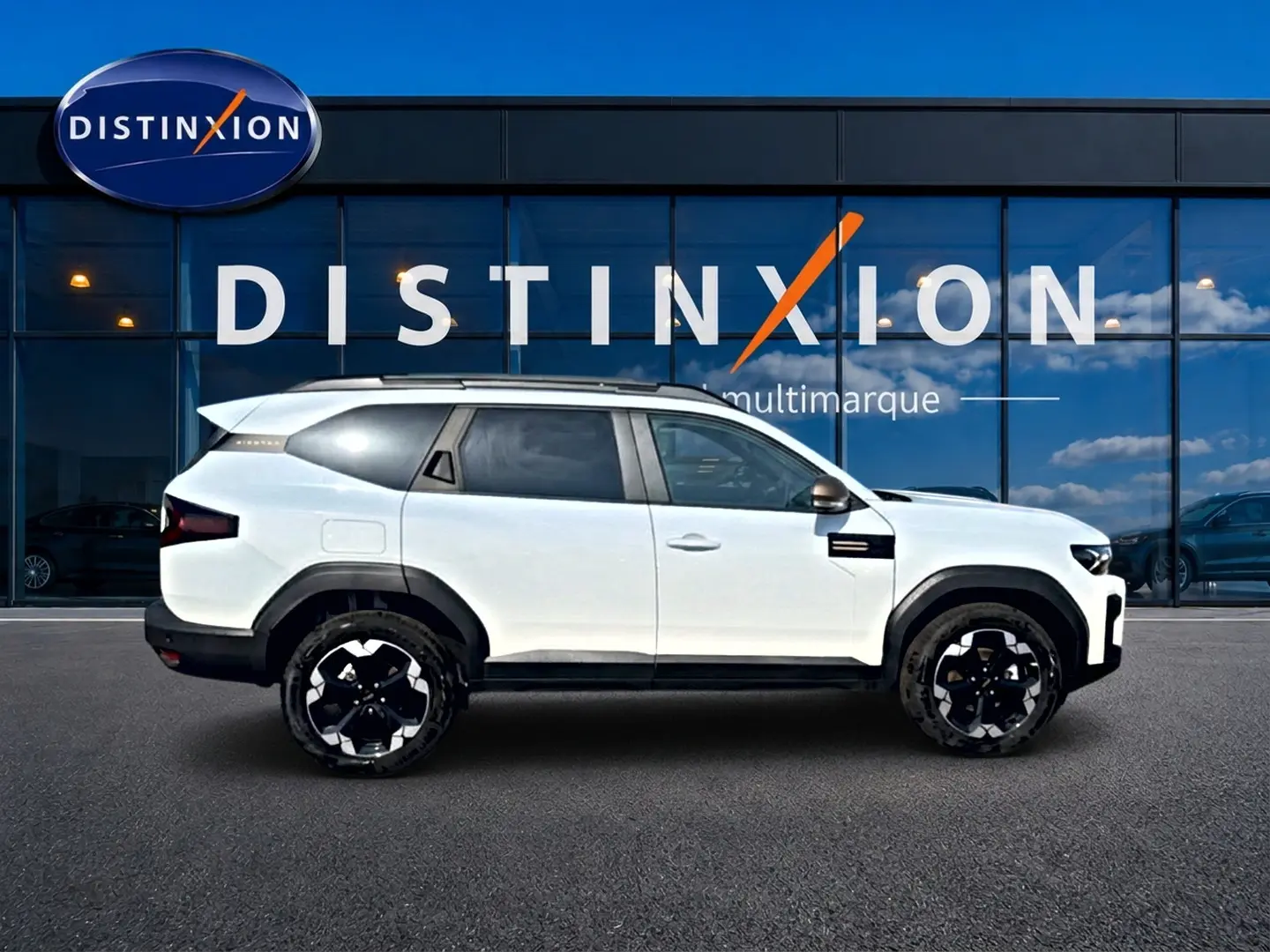 Profil droit du SUV blanc Dacia Bigster 2026 avec jantes noires et détails noirs contrastants, devant une vitrine Distinxion.