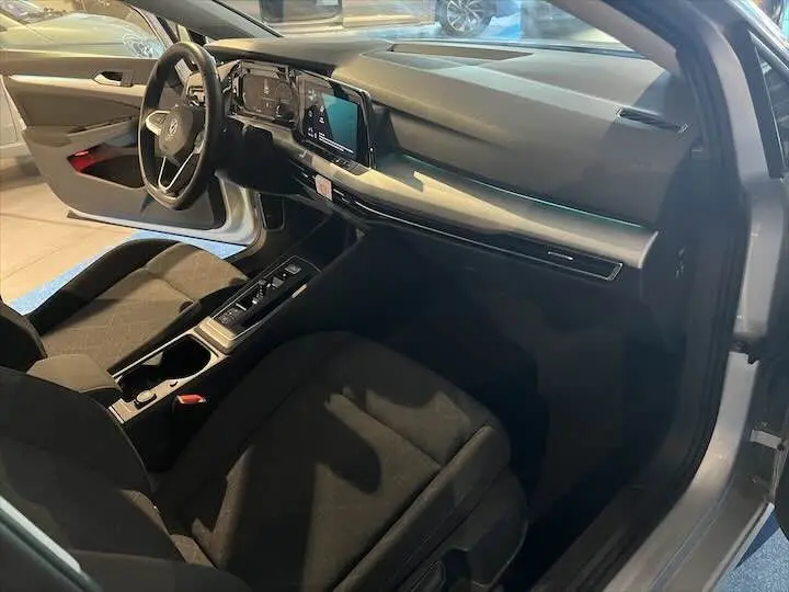 Intérieur de Volkswagen Golf 8 essence, vue côté conducteur avec sièges noirs et tableau de bord moderne en reflet argent métal.