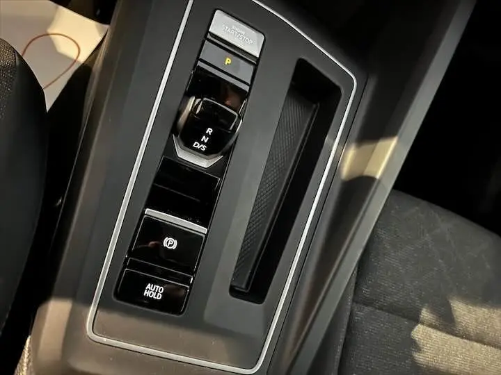 Gros plan sur la console centrale noire de la Volkswagen Golf 8 avec levier de vitesses automatique et boutons de contrôle.