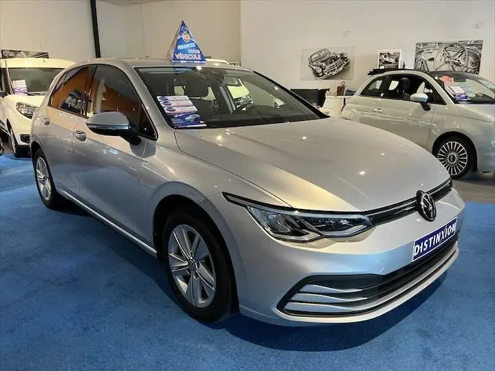 Volkswagen Golf 8 argent métal vue 3/4 avant en intérieur avec logo Distinxion sur le pare-chocs.