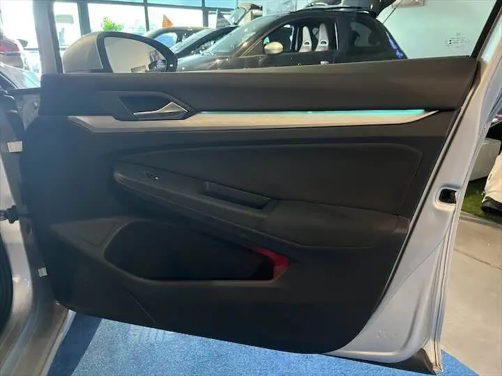 Vue rapprochée de la porte avant gauche ouverte d'une Volkswagen Golf 8 argent métallisé, intérieur noir avec détails argentés.