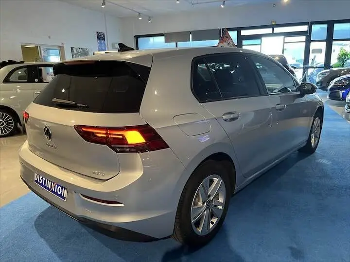 Volkswagen Golf 8 argent métal vue 3/4 arrière droit en intérieur avec feux arrière allumés.