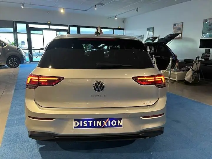 Vue arrière d'une Volkswagen Golf 8 essence couleur reflet d'argent métal avec feux allumés en showroom