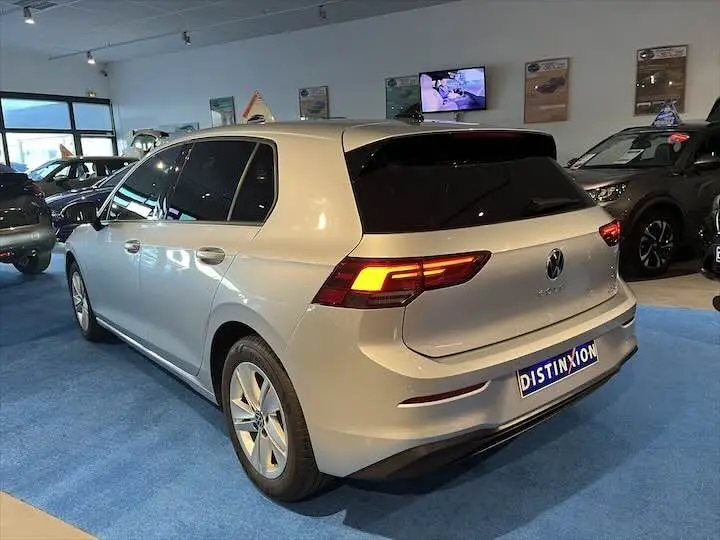 Volkswagen Golf 8 argent métal vue 3/4 arrière droit en intérieur avec feux arrière allumés et plaque Distinxion.