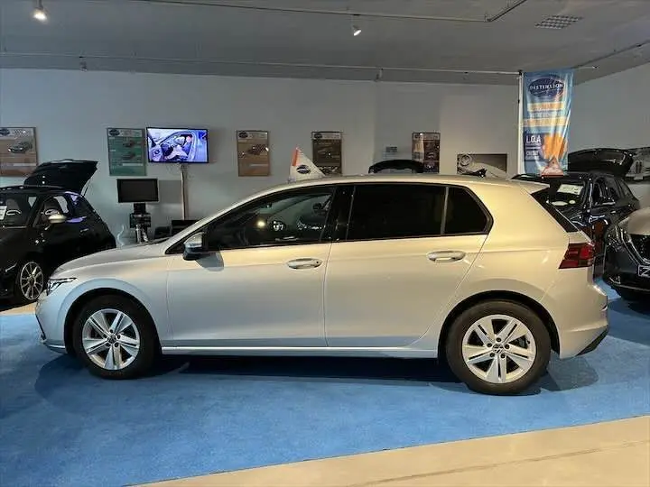Volkswagen Golf 8 argent métal vue de profil côté gauche en intérieur sur sol bleu dans un showroom.