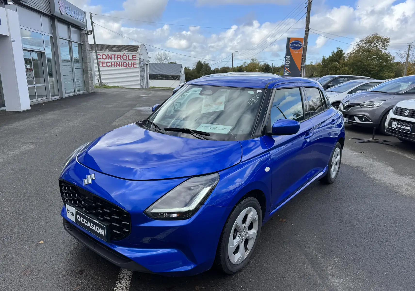 Vue 3/4 avant droite d'une Suzuki Swift bleu vif 2025 hybride, avec calandre noire et phares LED distinctifs.