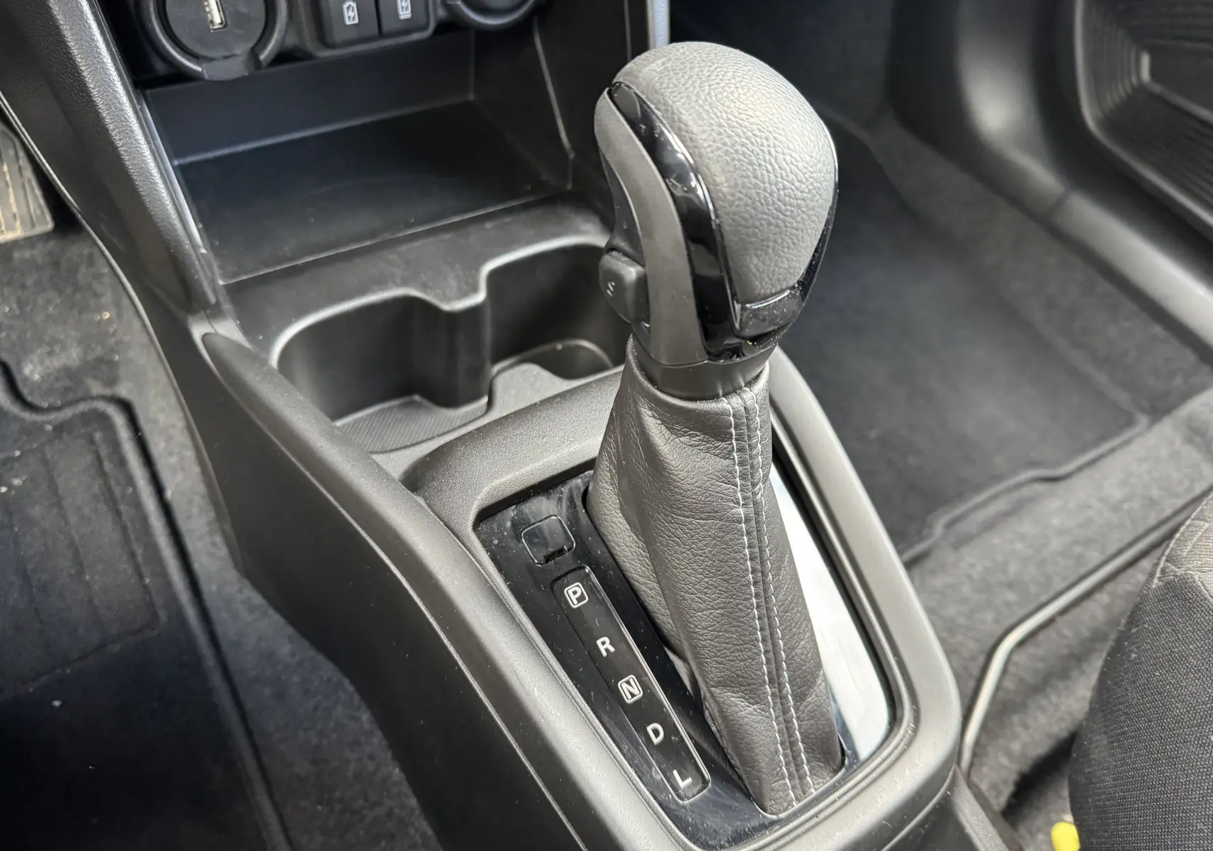 Gros plan sur la commande de boîte automatique noire dans l'habitacle d'une Suzuki Swift 1.2 Hybrid Privilege.