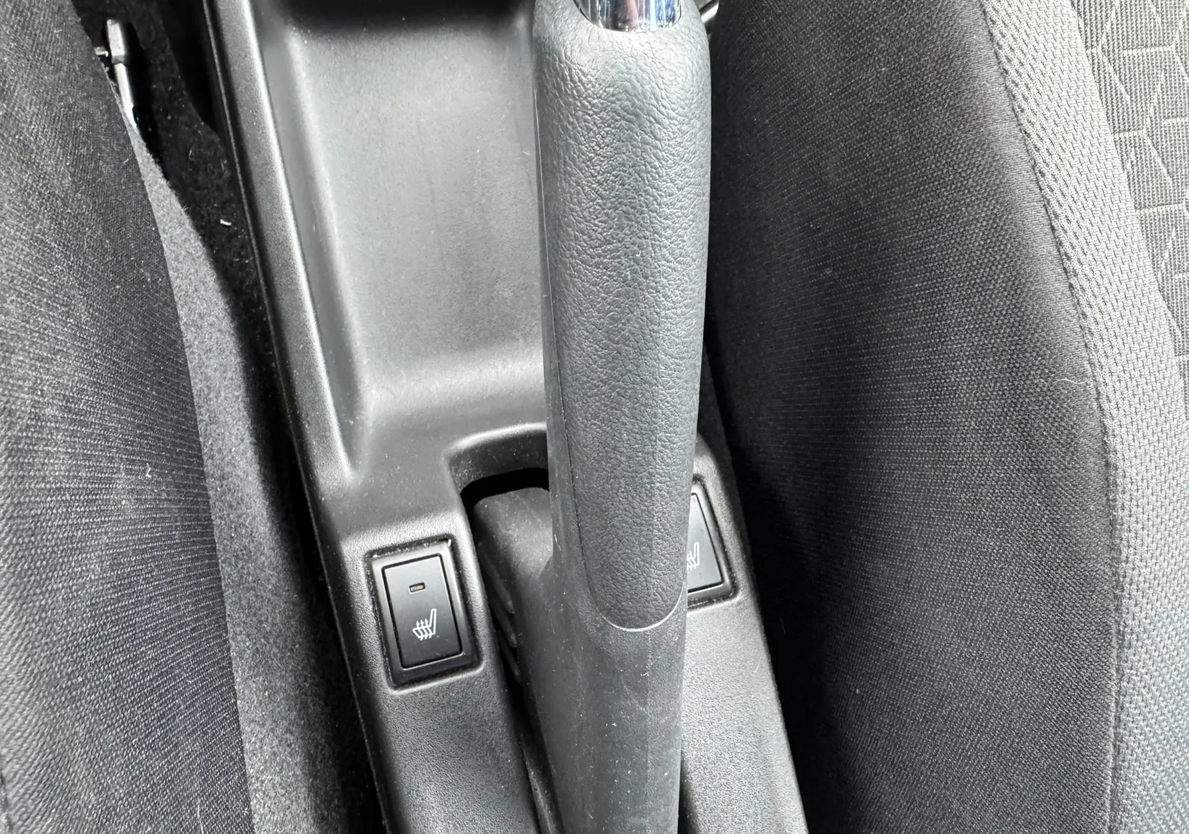 Vue rapprochée de la commande de frein à main et des boutons de sièges chauffants dans une Suzuki Swift bleu 2025.