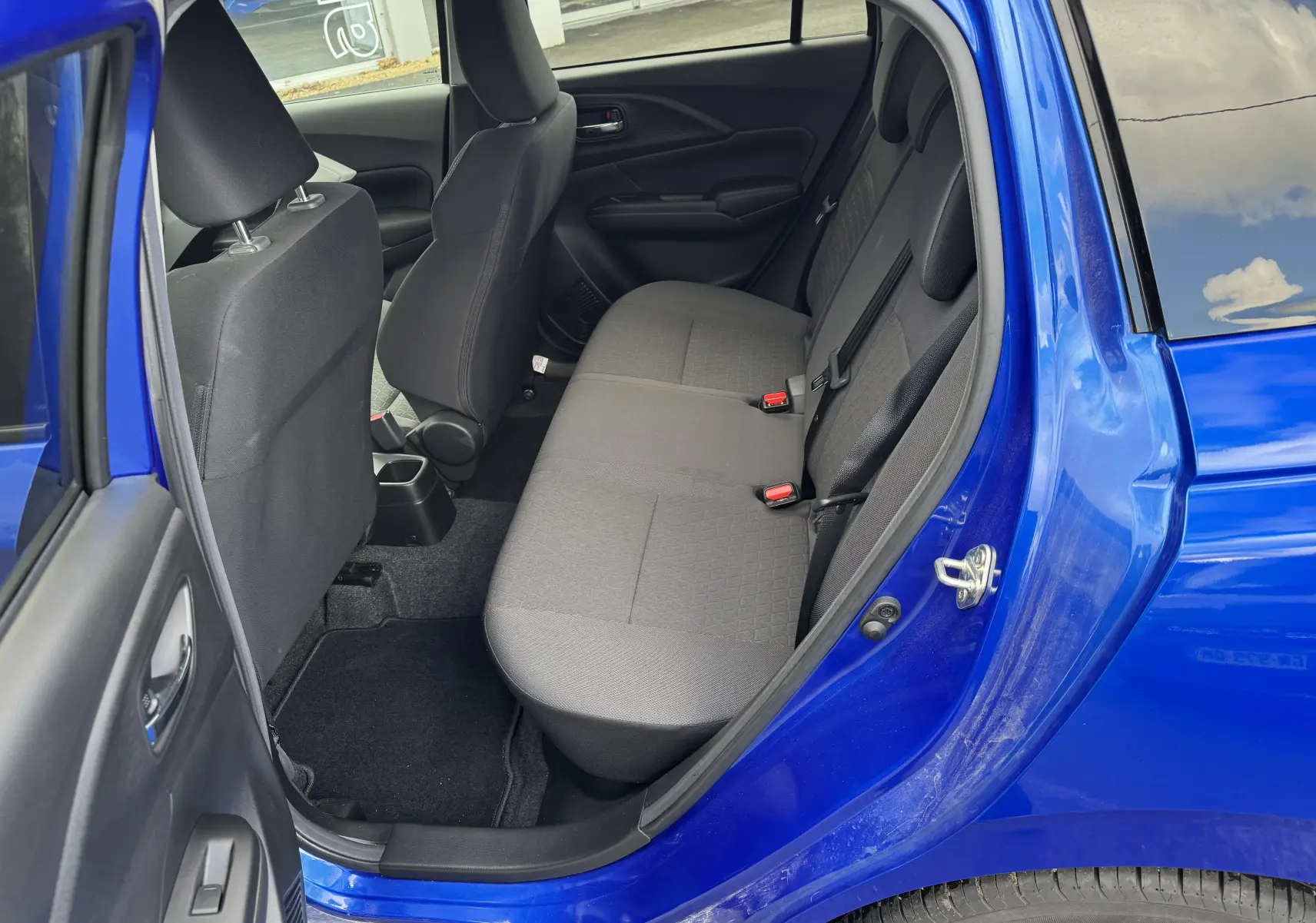 Vue intérieure côté droit sur la banquette arrière grise d'une Suzuki Swift 1.2 Hybrid Privilege Auto bleue 2025, porte ouverte.