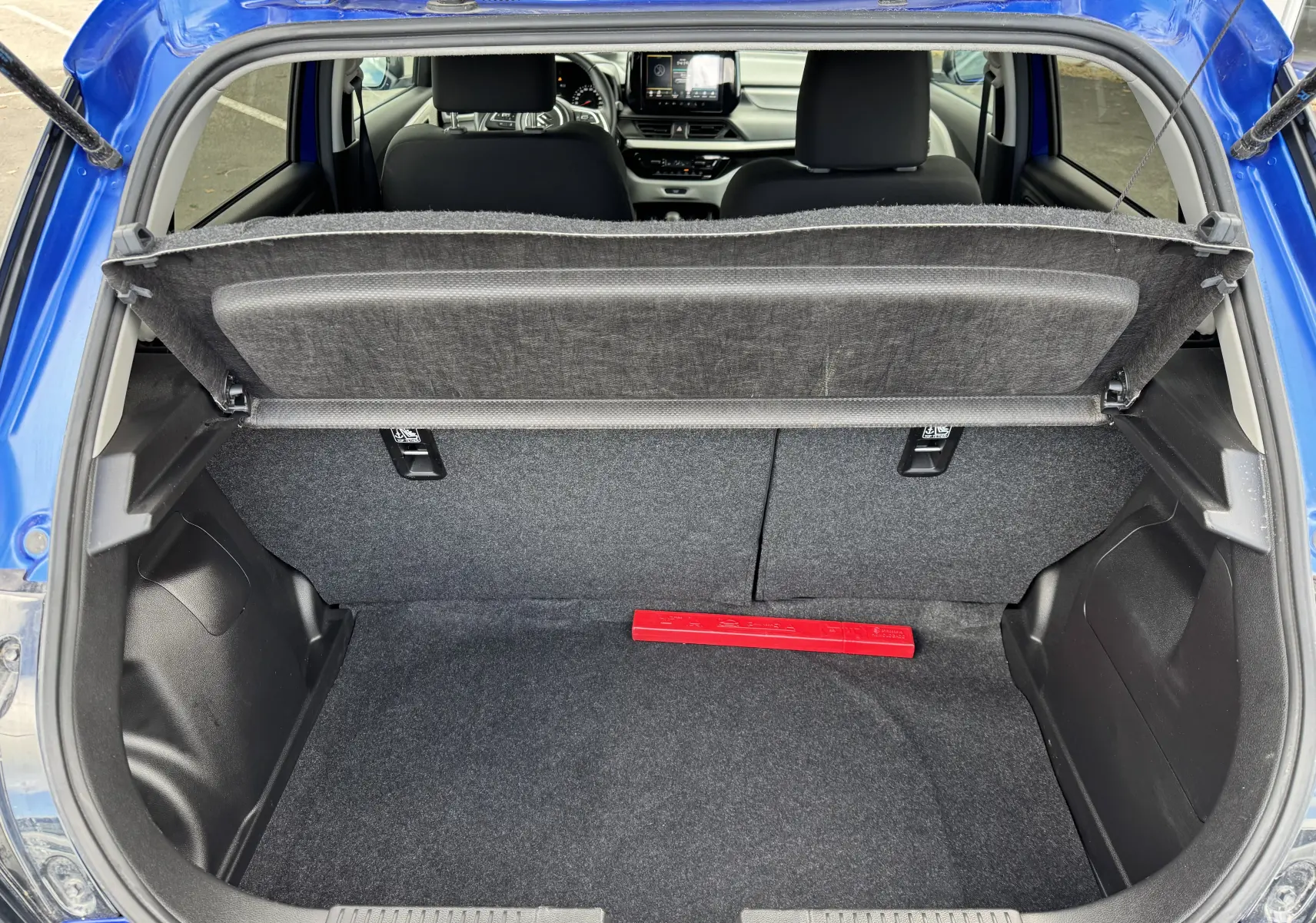 Coffre ouvert vu de l'arrière d'une Suzuki Swift bleu 2025, avec tablette de séparation et intérieur noir.