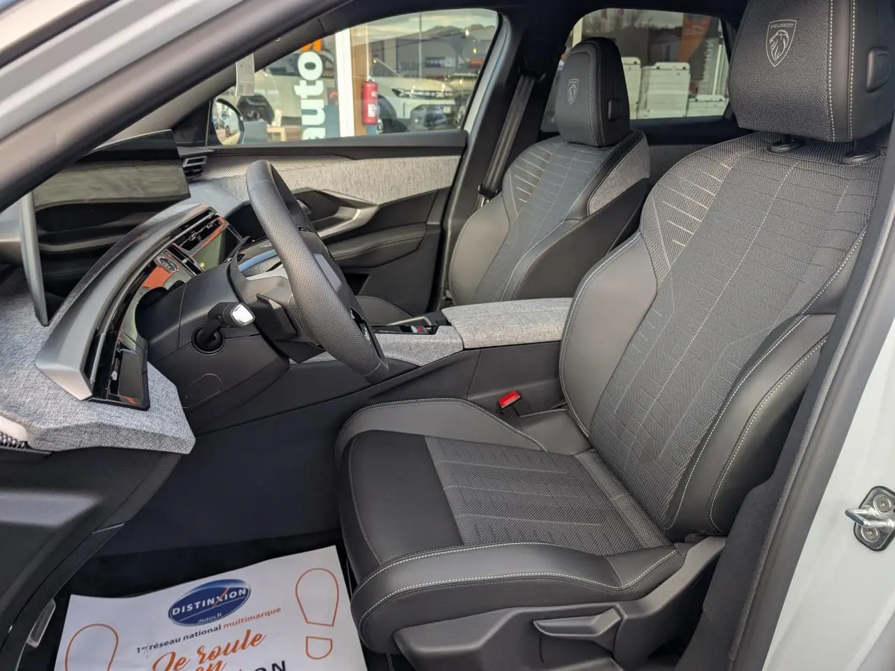 Vue intérieure côté conducteur du Peugeot 3008 blanc 2025, sièges tissu et cuir avec logo Peugeot brodé sur appuie-tête.