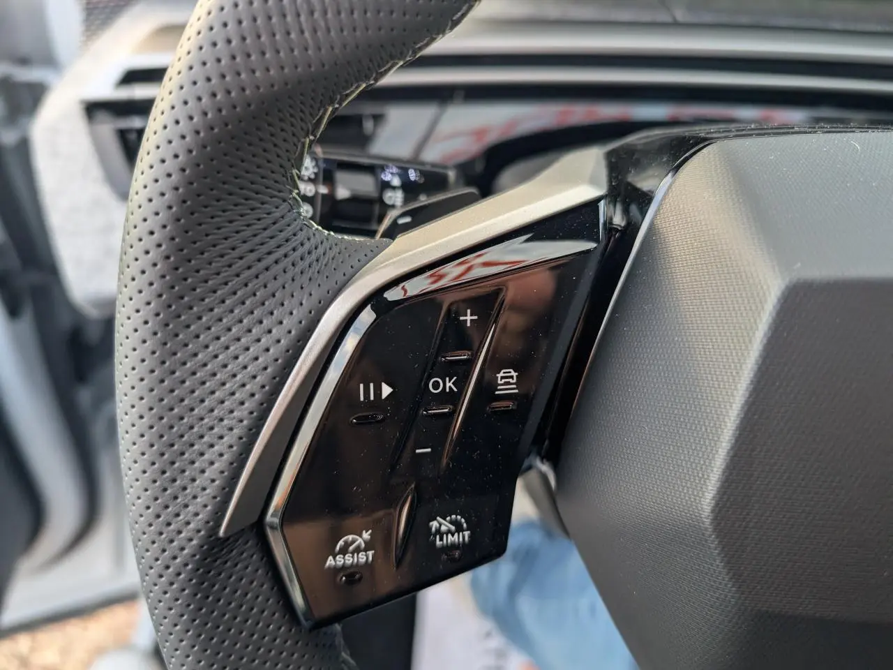 Gros plan sur les commandes gauche du volant perforé noir laqué du Peugeot 3008 blanc hybride 2025 GT