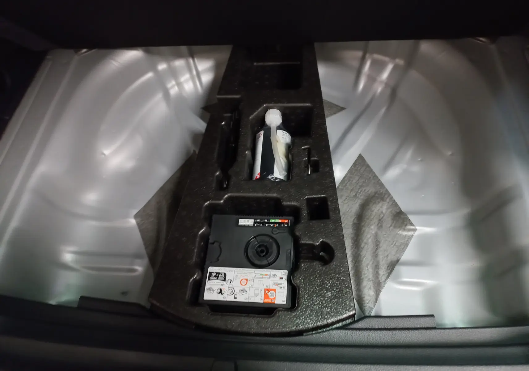 Gros plan sur le coffre du Skoda Karoq 2025 gris argent, montrant le plancher de chargement variable et le kit de réparation.