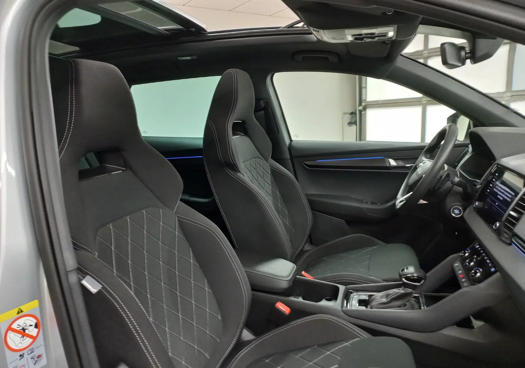 Vue intérieure côté conducteur du Skoda Karoq gris argent 2025, sièges sport noirs et toit panoramique ouvrant en verre.