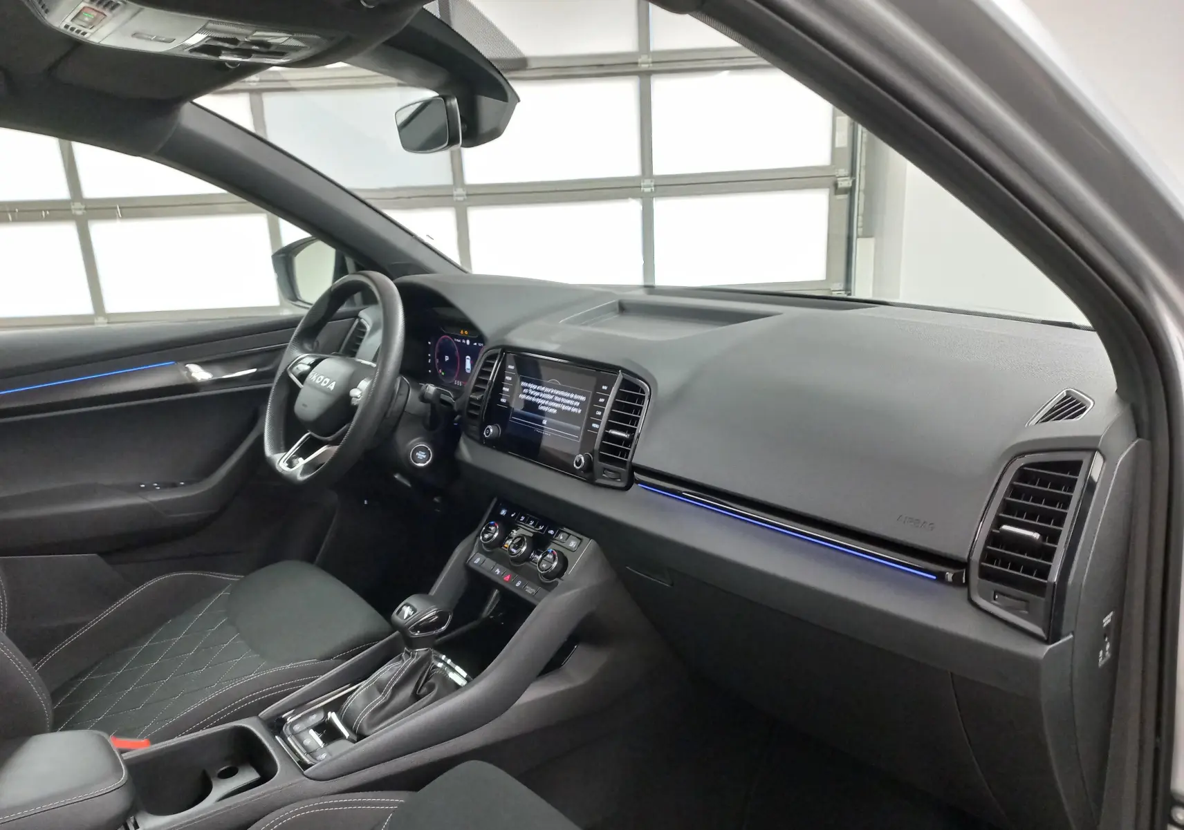 Intérieur du Skoda Karoq 2025 vu côté conducteur, avec tableau de bord moderne et éclairage d'ambiance bleu.