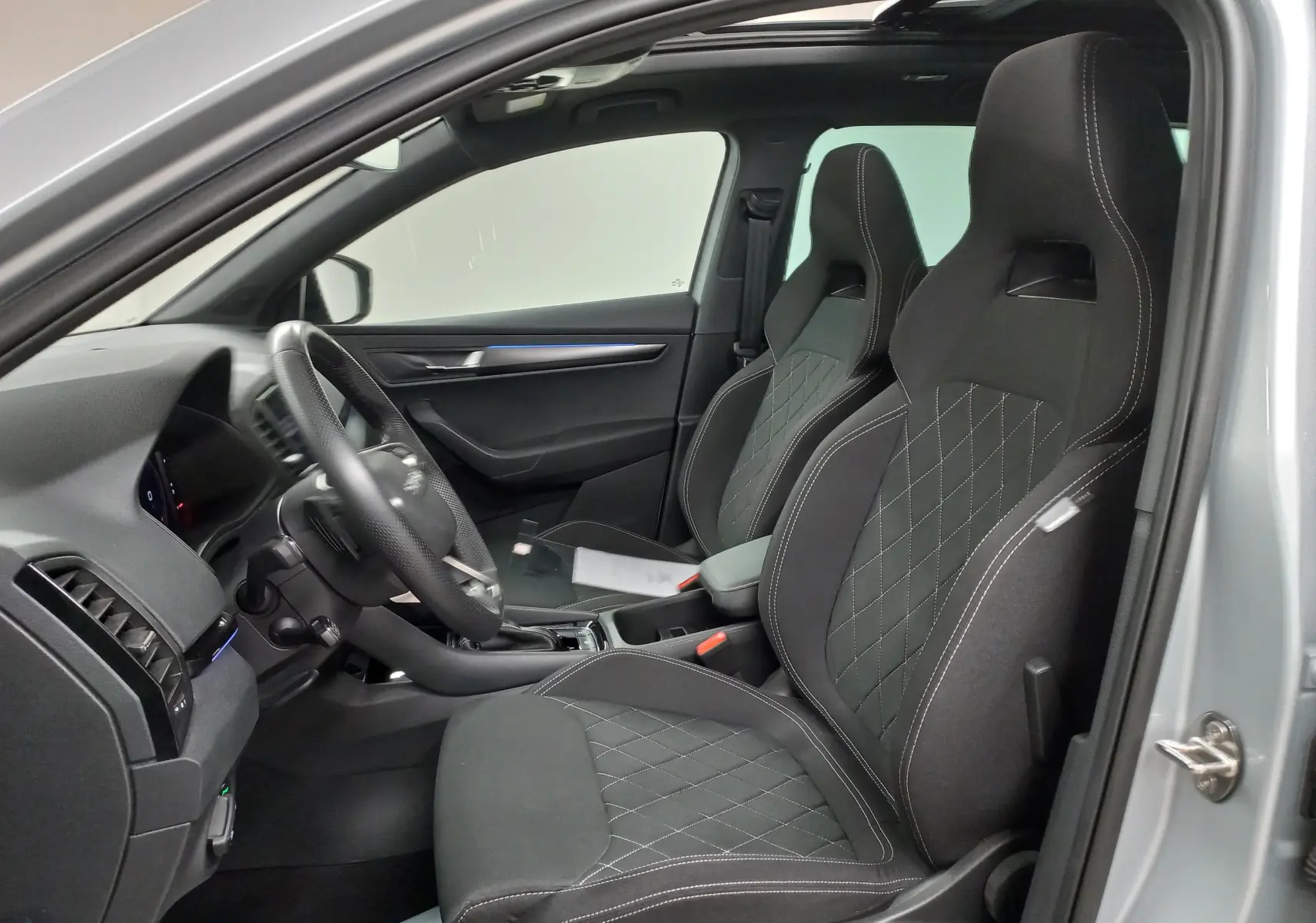 Vue intérieure côté conducteur du Skoda Karoq gris argent 2025, mettant en valeur les sièges sport noirs avec surpiqûres blanches.