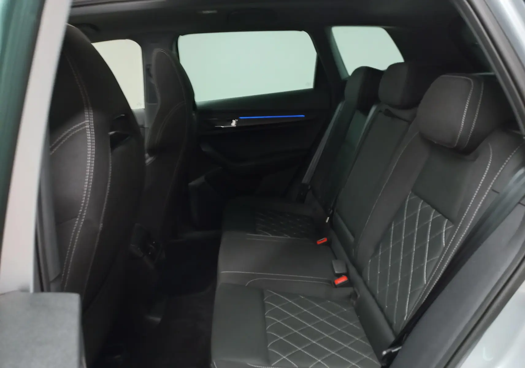 Vue intérieure côté gauche des sièges arrière noirs avec surpiqûres blanches du Skoda Karoq gris argent 2025.