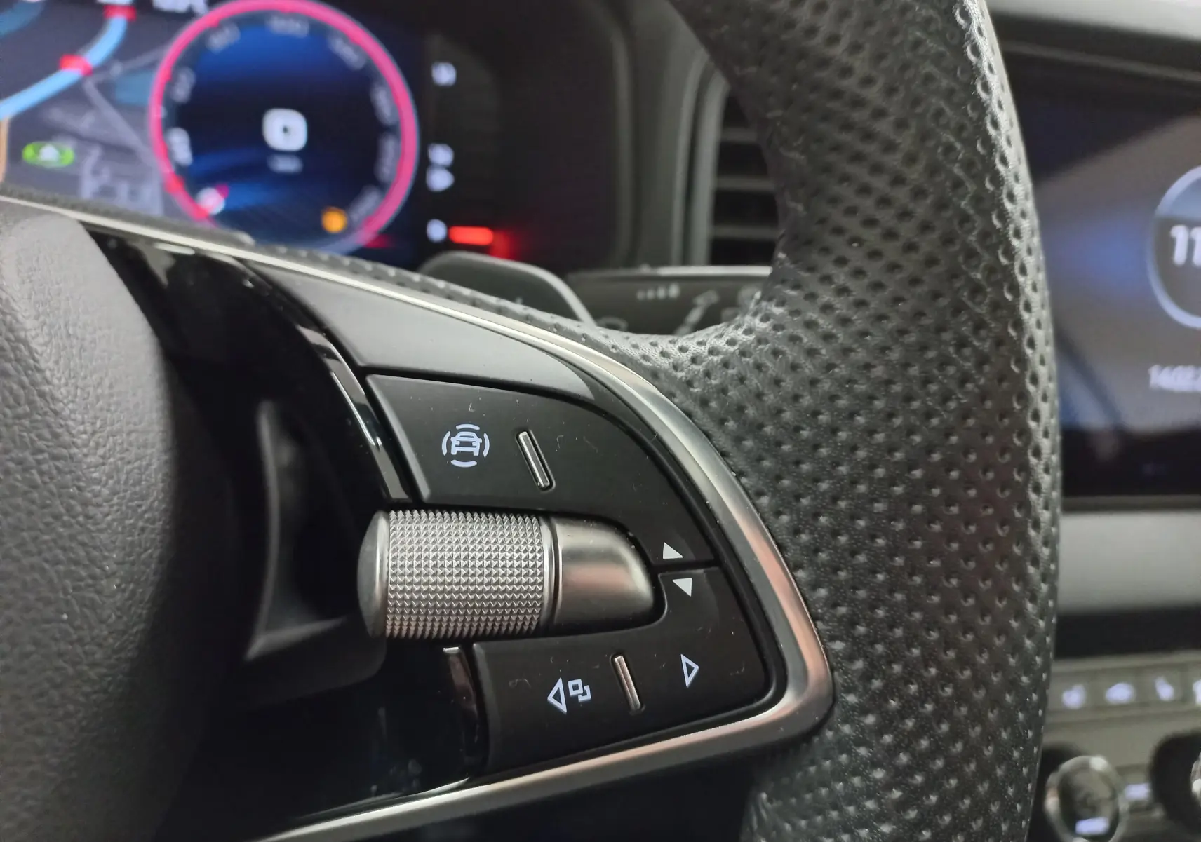 Gros plan sur la partie gauche du volant perforé du Skoda Karoq 2025 avec commandes intégrées et tableau de bord numérique flou.