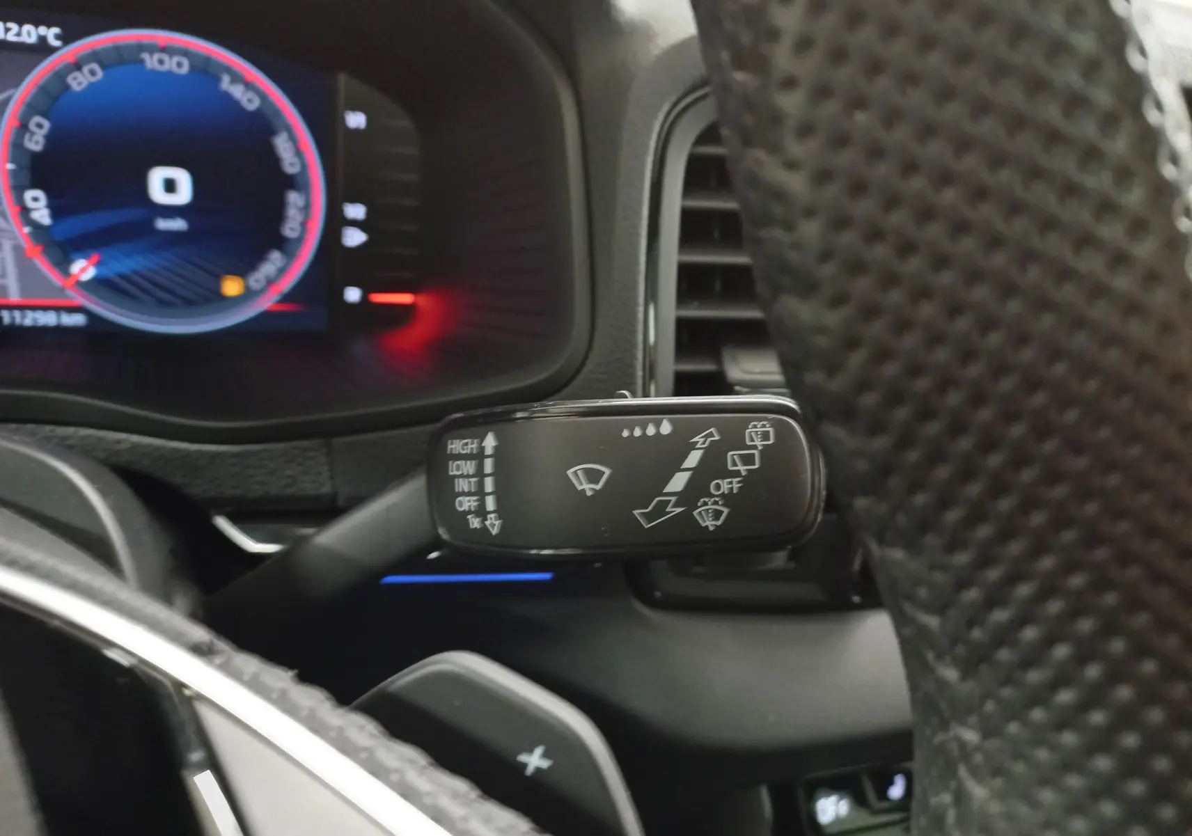 Gros plan sur le commodo d’essuie-glace à gauche du volant du Skoda Karoq gris argent, tableau de bord en arrière-plan.