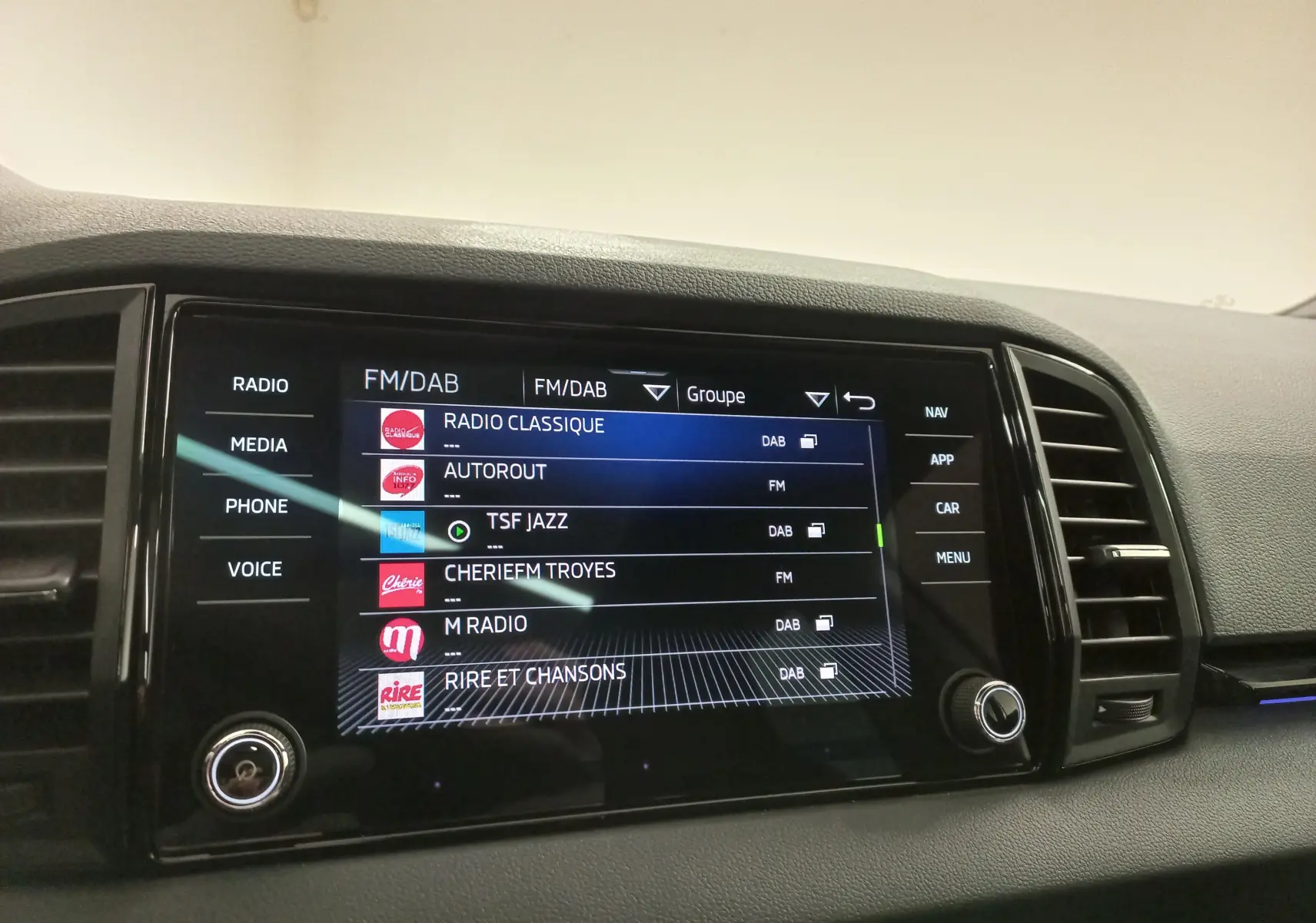 Écran tactile central du Skoda Karoq 2025 affichant les options radio FM/DAB, entouré de commandes noires et grises.