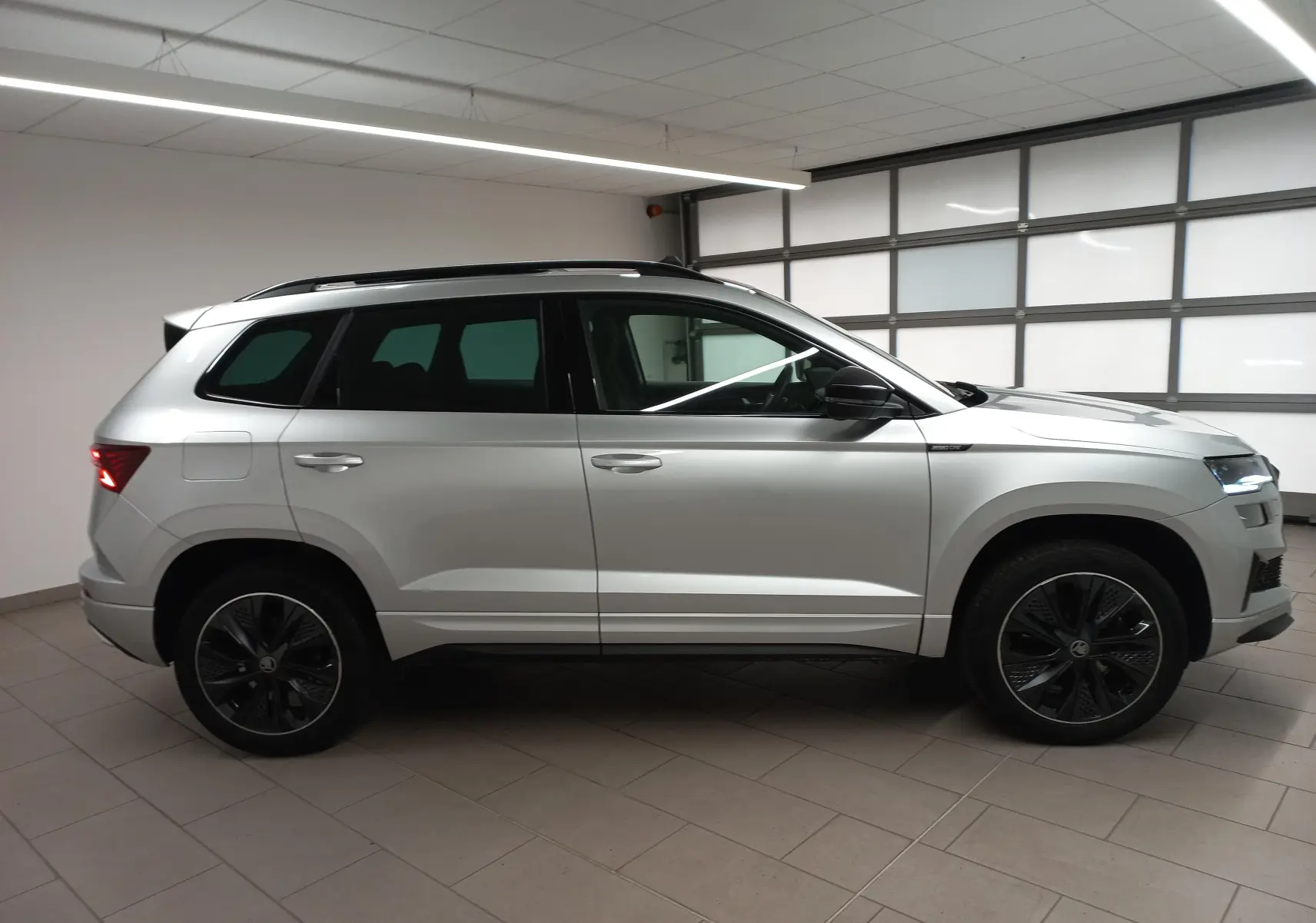 Vue de profil côté gauche du Skoda Karoq gris argent 2025 avec toit panoramique et jantes noires sportline.