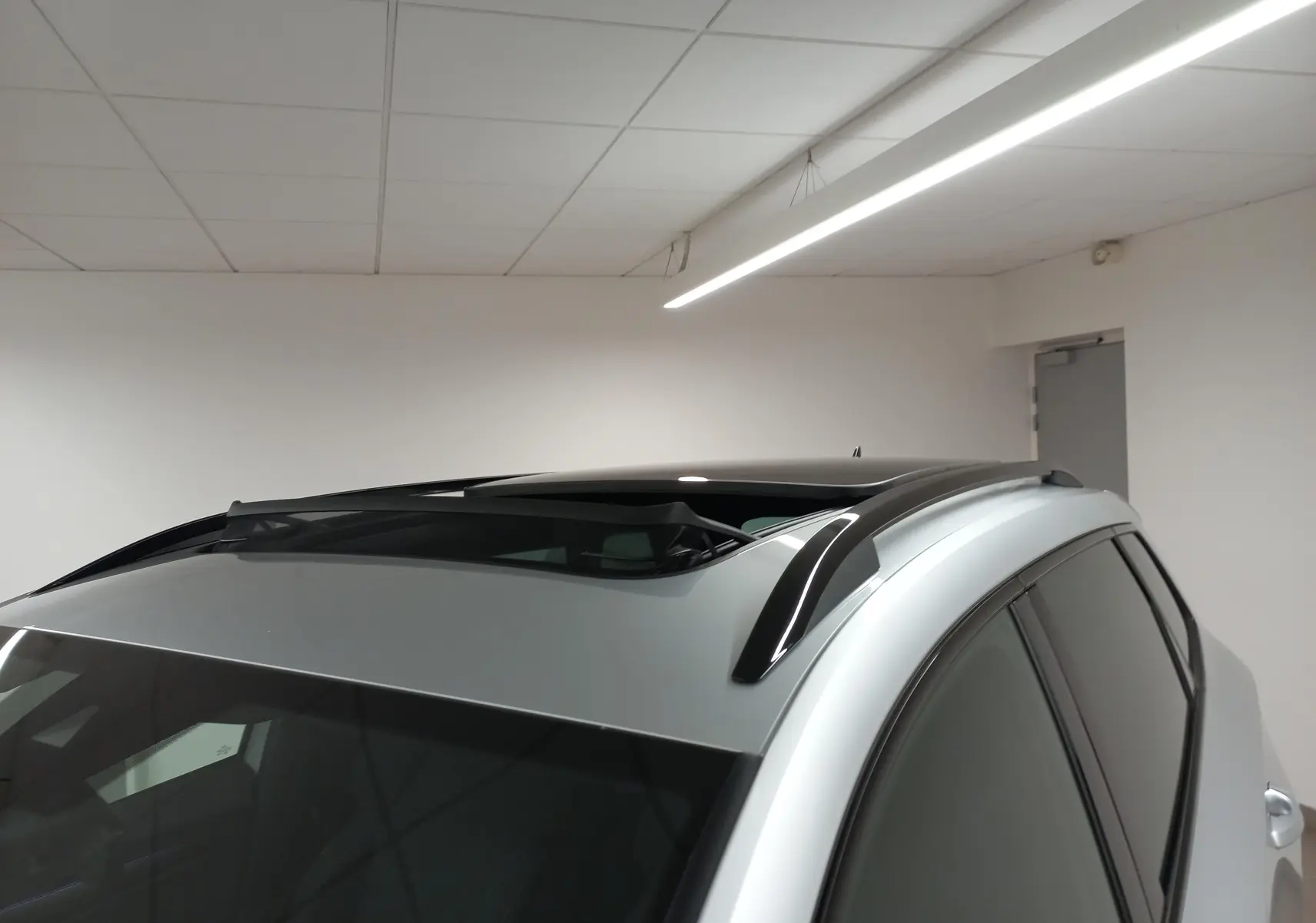 Vue rapprochée du toit ouvrant panoramique en verre du Skoda Karoq gris argent, avec barres de toit noires visibles.