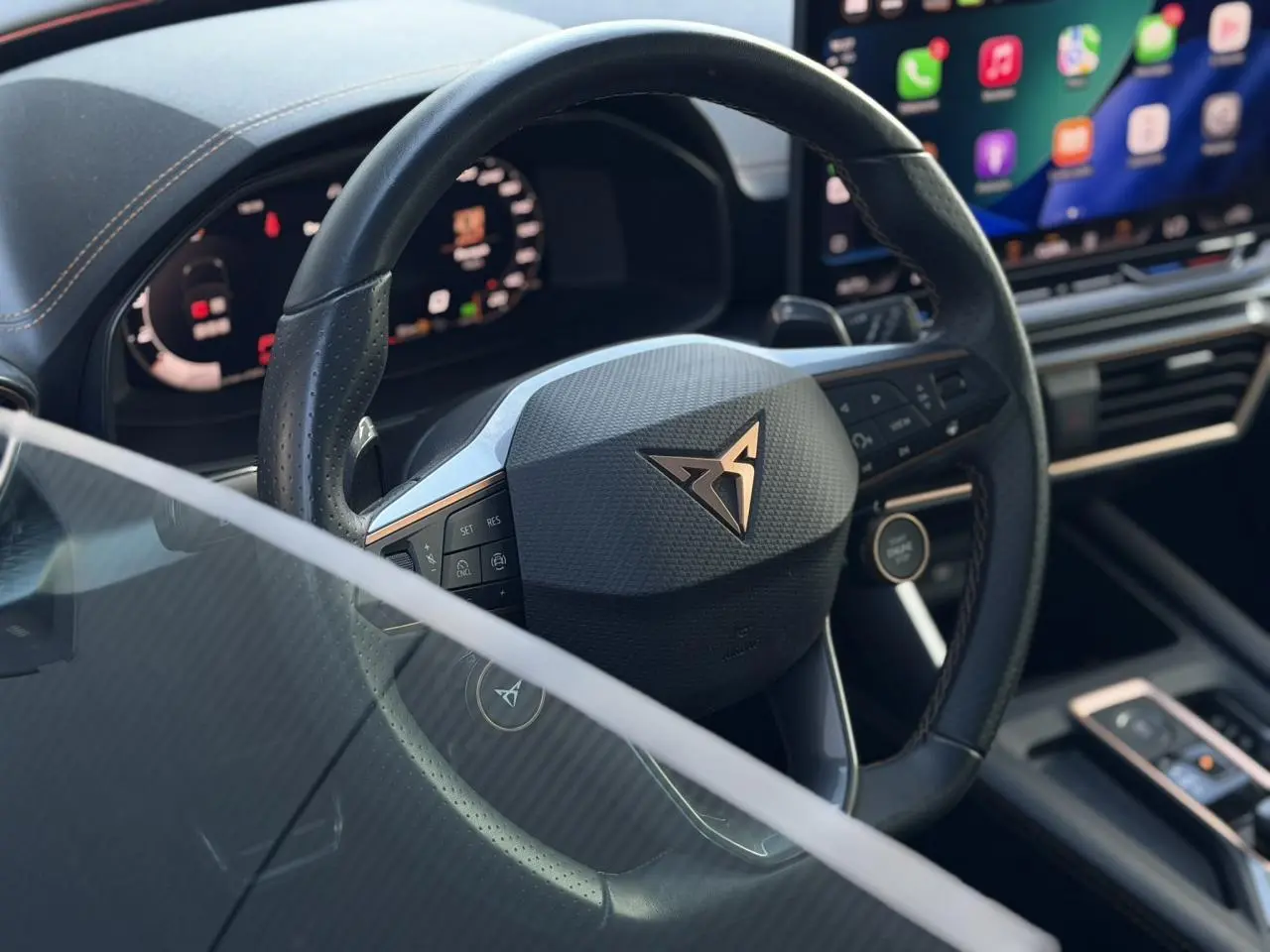 Vue rapprochée du volant cuir noir perforé avec logo CUPRA, tableau de bord digital et écran tactile lumineux.