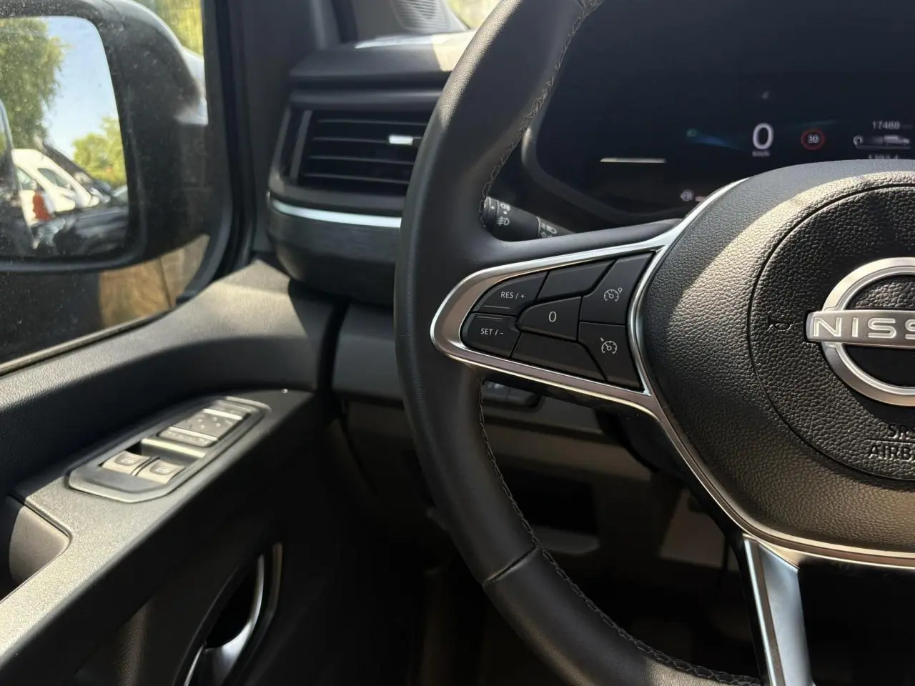 Vue intérieure côté conducteur du Nissan Primastar Combi 2025, volant multifonctions et commandes lève-vitres sur portière noire.