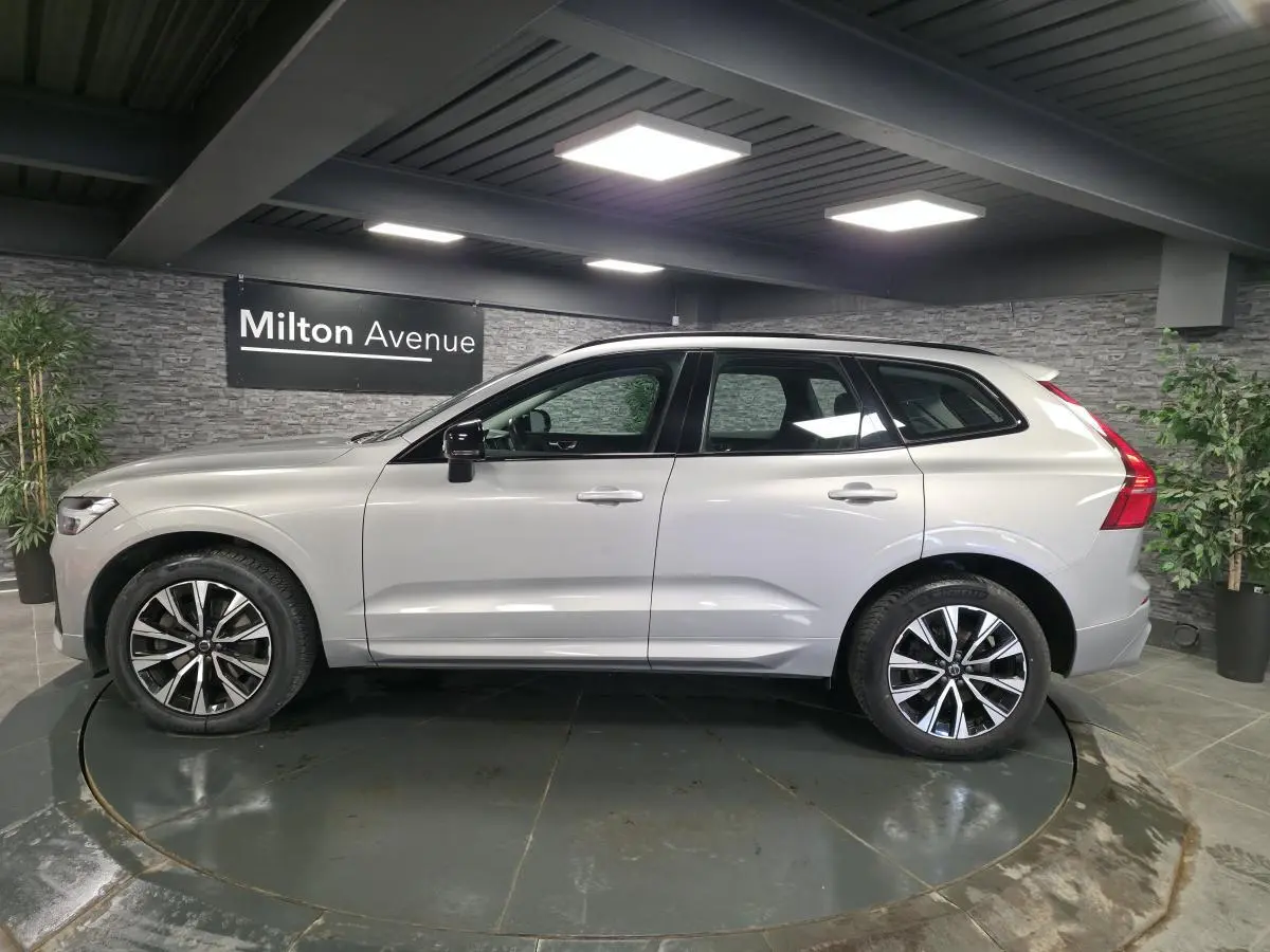 Volvo XC60 gris vue de profil côté gauche, avec jantes alliage noires et toit ouvrant panoramique visible.