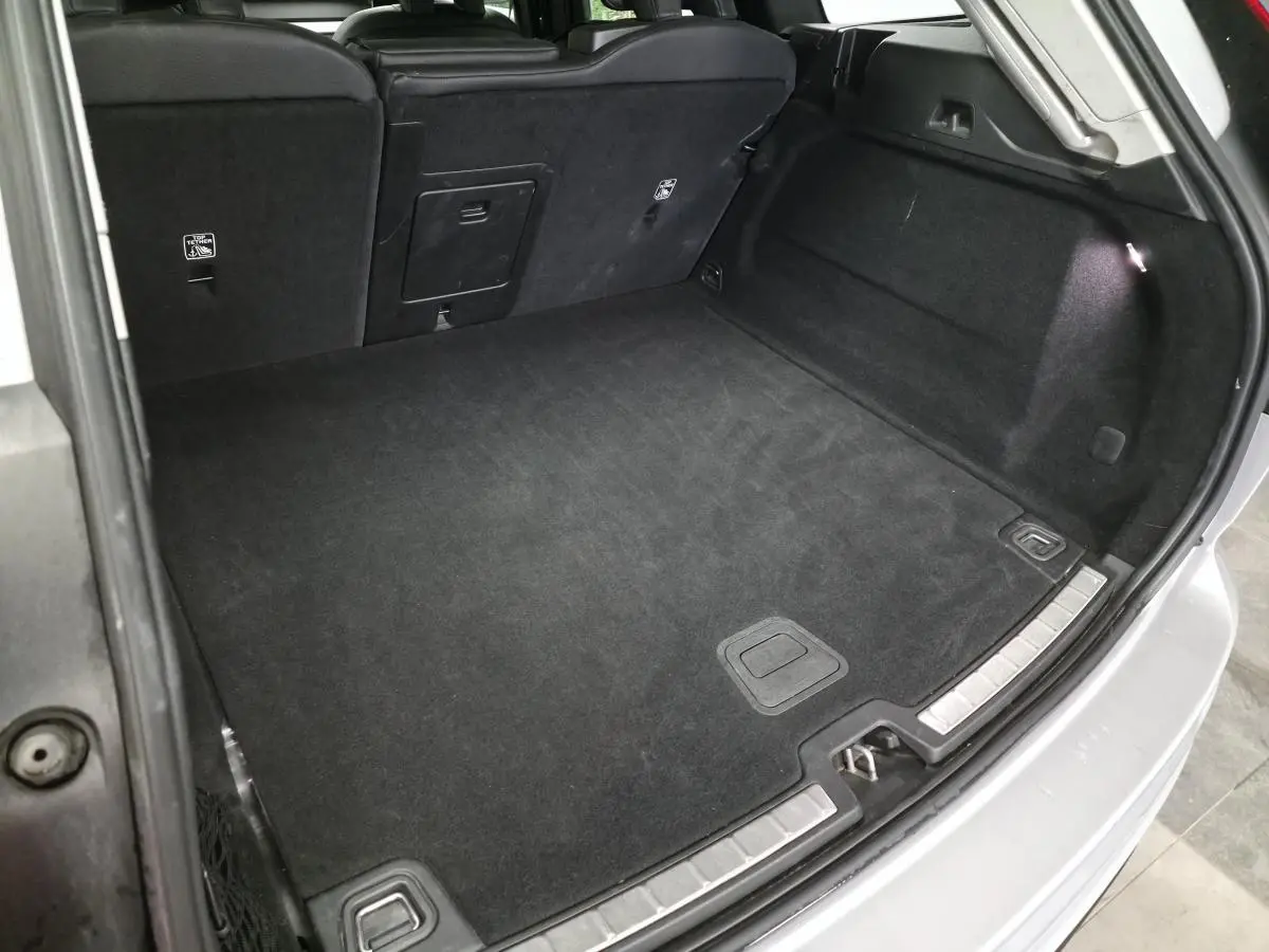 Coffre spacieux ouvert du Volvo XC60 gris 2023, avec tapis noir et éclairage intérieur visible.