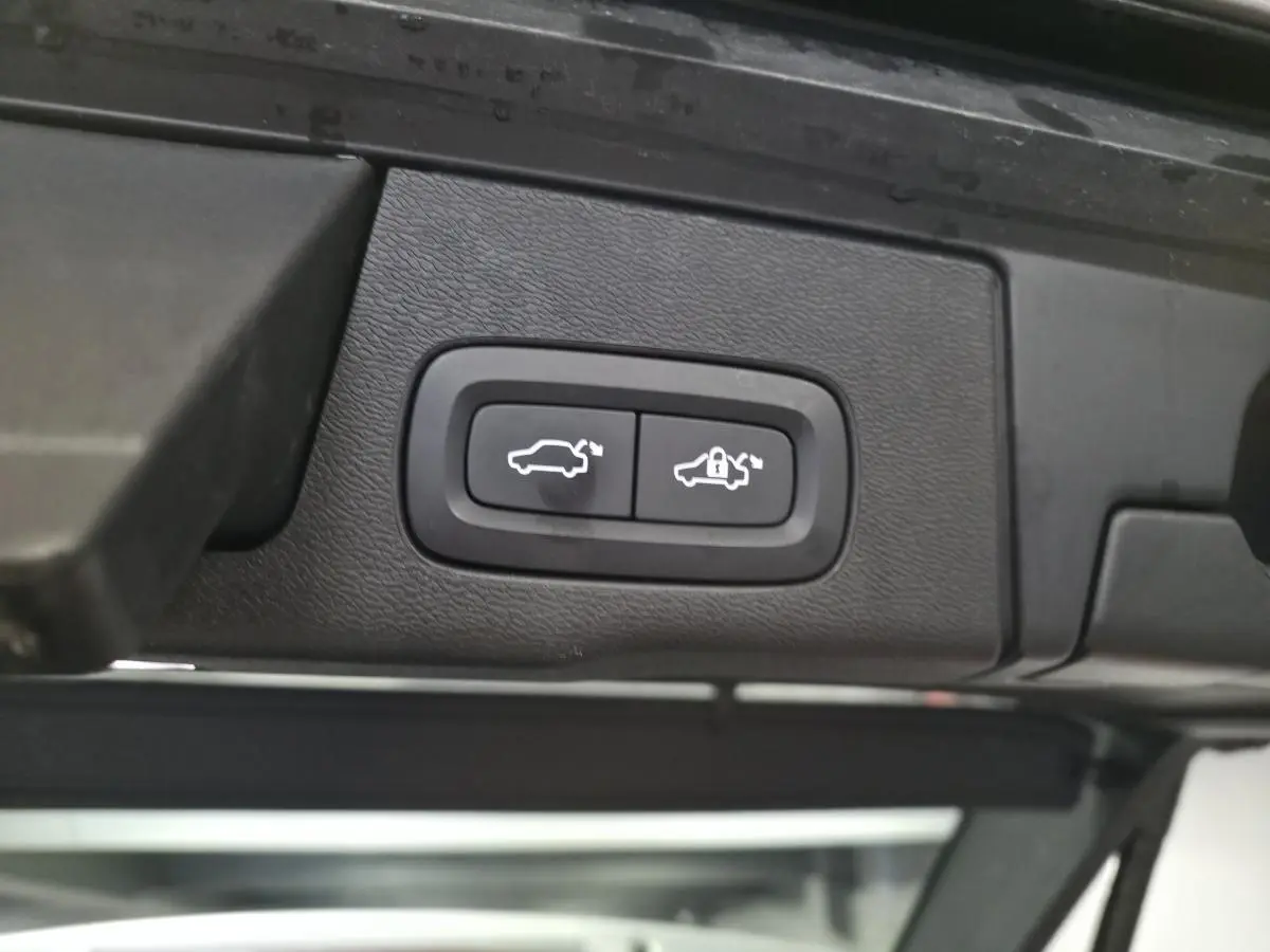 Boutons d'ouverture et de verrouillage du hayon électrique sur le bord intérieur du coffre d'un Volvo XC60 gris.