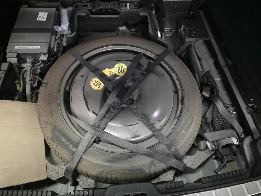 Vue plongeante sur la roue de secours temporaire grise fixée dans le coffre du Volvo XC60 gris 2023.