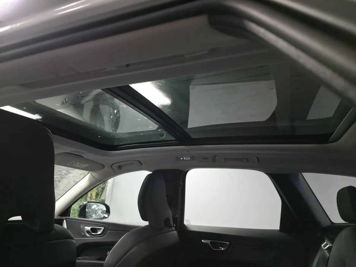 Vue intérieure du toit ouvrant panoramique en verre du Volvo XC60 gris, montrant les sièges avant et arrière noirs.